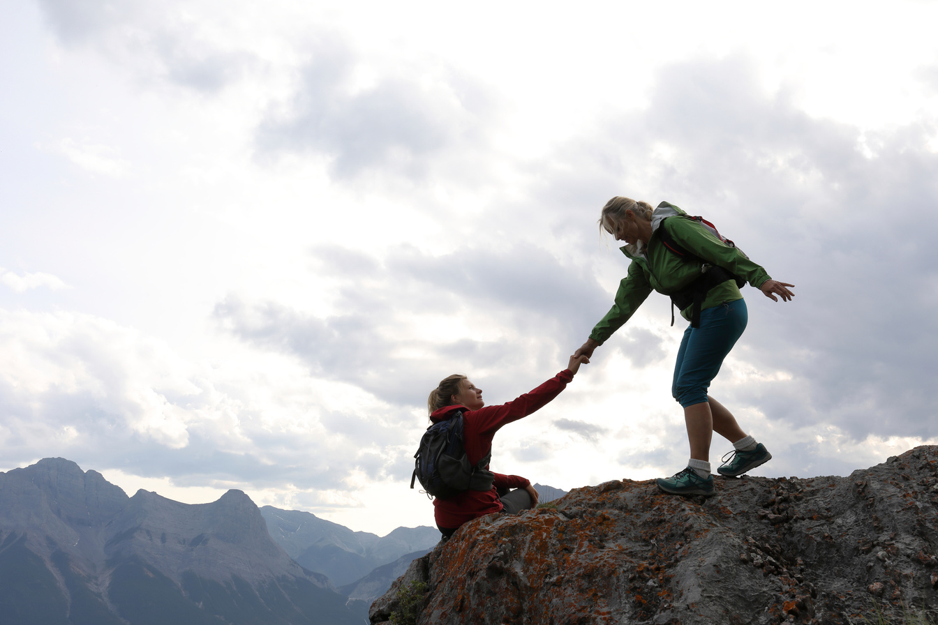 Female climbers helping each other up a mountain